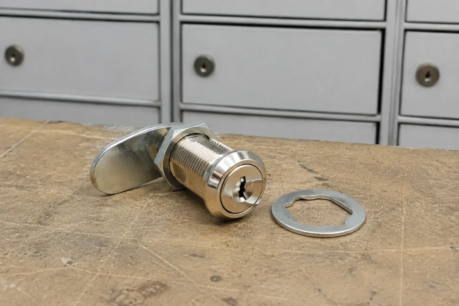 Detached threaded cam lock and mounting washer on a workbench in front of closed mail compartments. — Mailbox Lock Replacement, Halton Hills