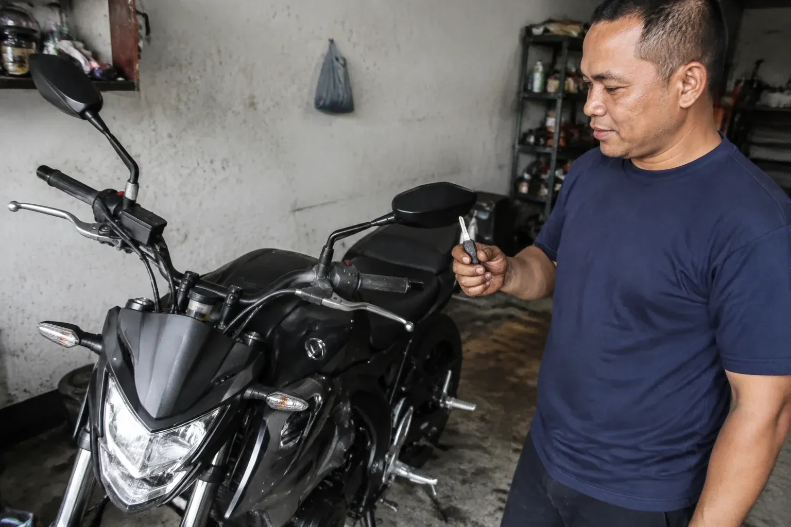 Person holding a key beside a black motorcycle in a garage. — Motorcycle & Scooter Keys, Halton Hills
