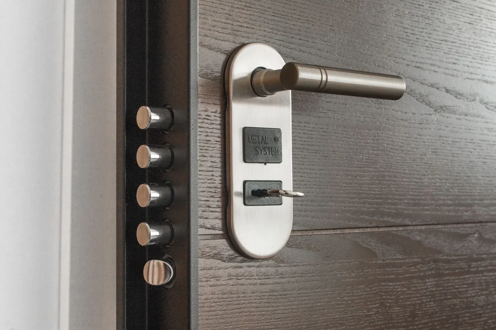 Steel door lever on an oval plate with a key in the lock, beside a row of metal bolts on the edge. — Halton Hills