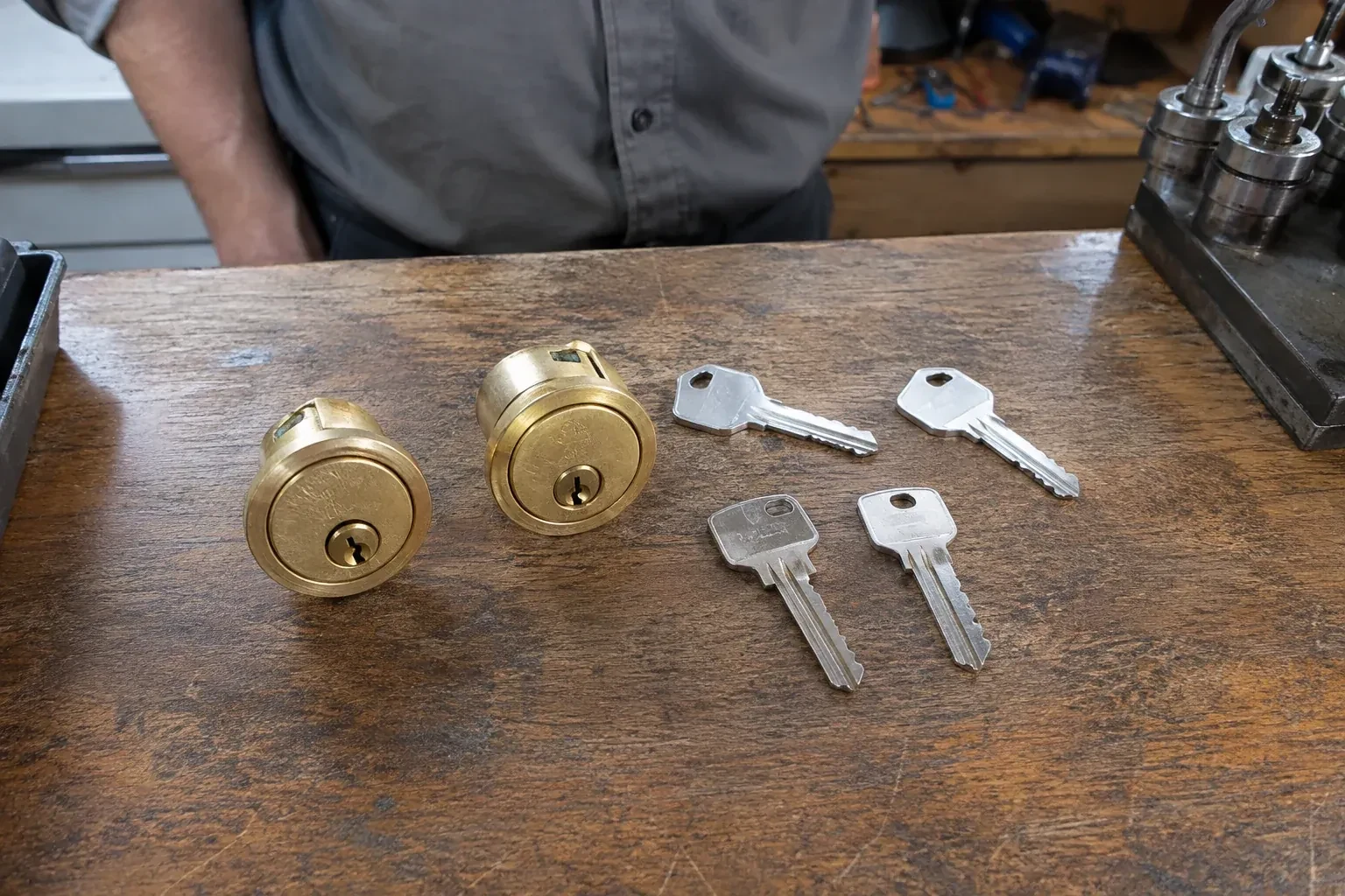 Two detached brass lock cylinders and four house keys on a wooden counter. — Lock Rekeying, Halton Hills